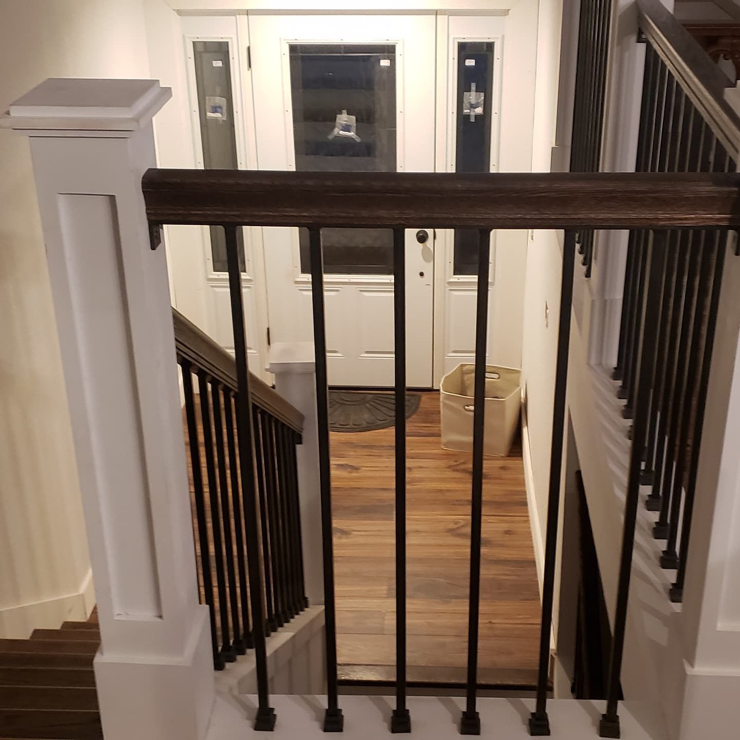 View down staircase with brown wood railing, black iron spindles, and white trim; doorway at end.