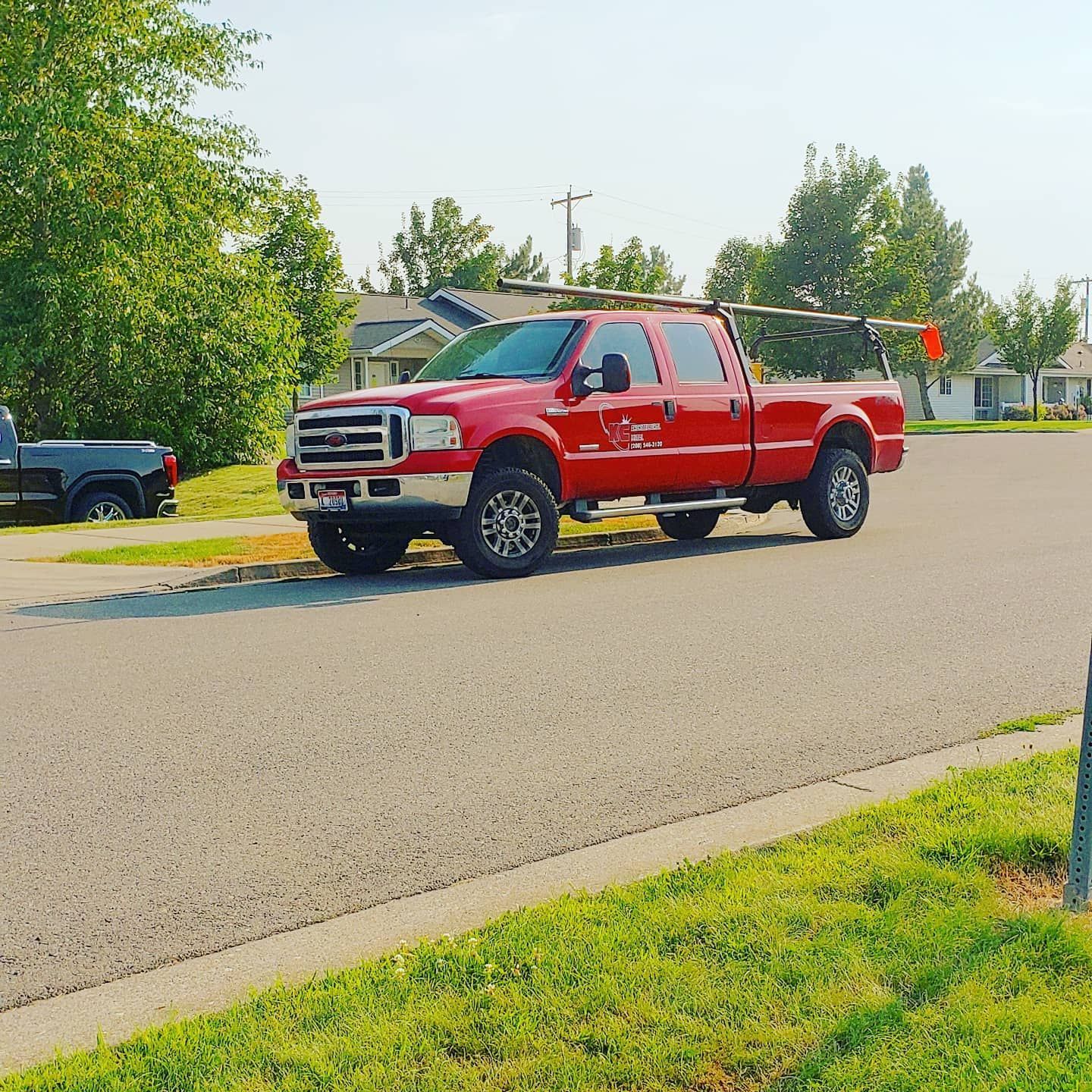 Red work truck parked on a residential street; trees and houses in the background.