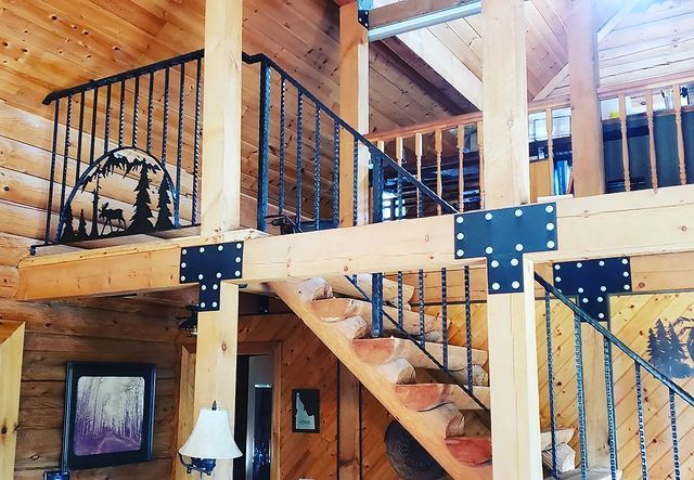 Wooden interior with stairs and black metal railings, a mountain and tree silhouette on railing.