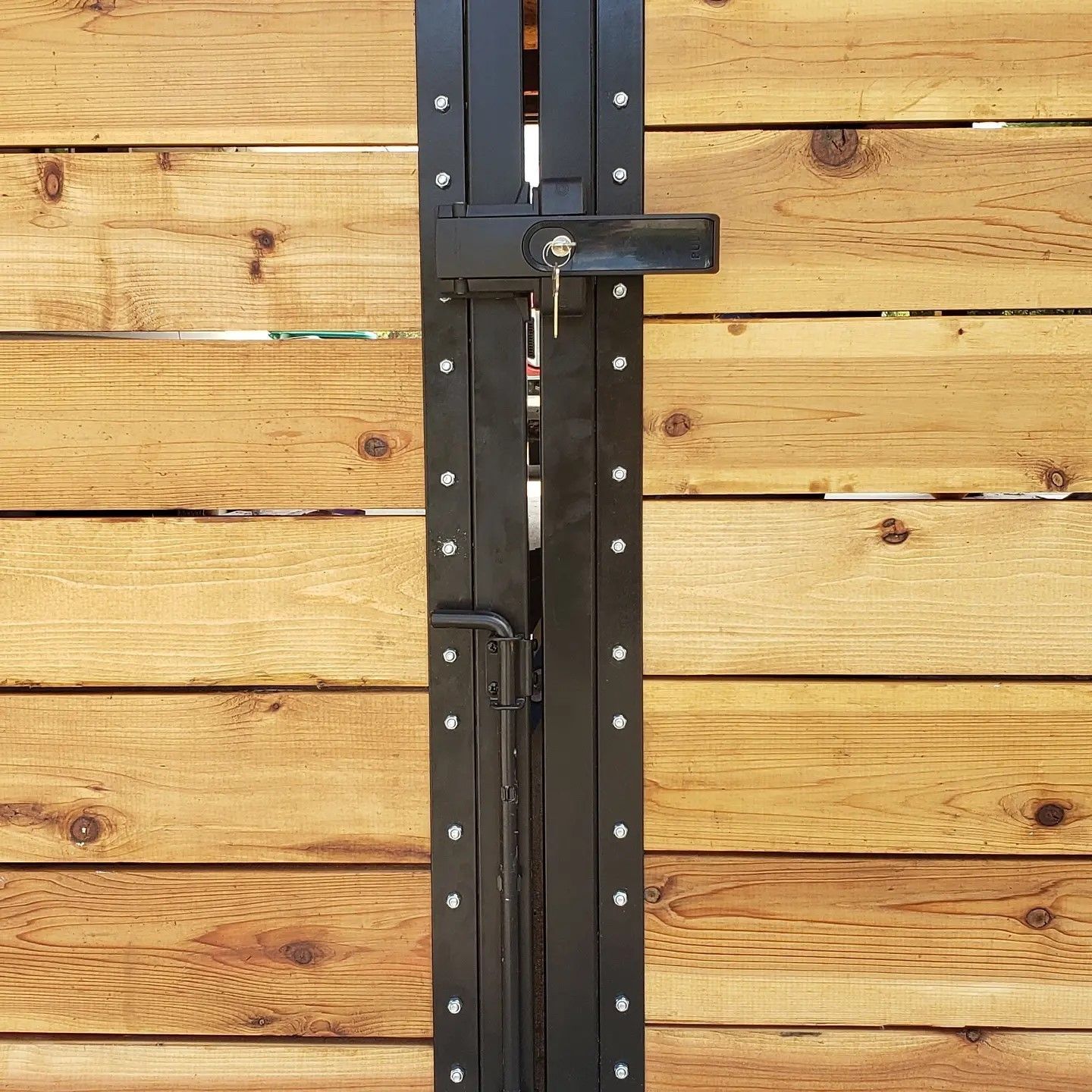 Black metal gate with a key lock on a wooden fence.
