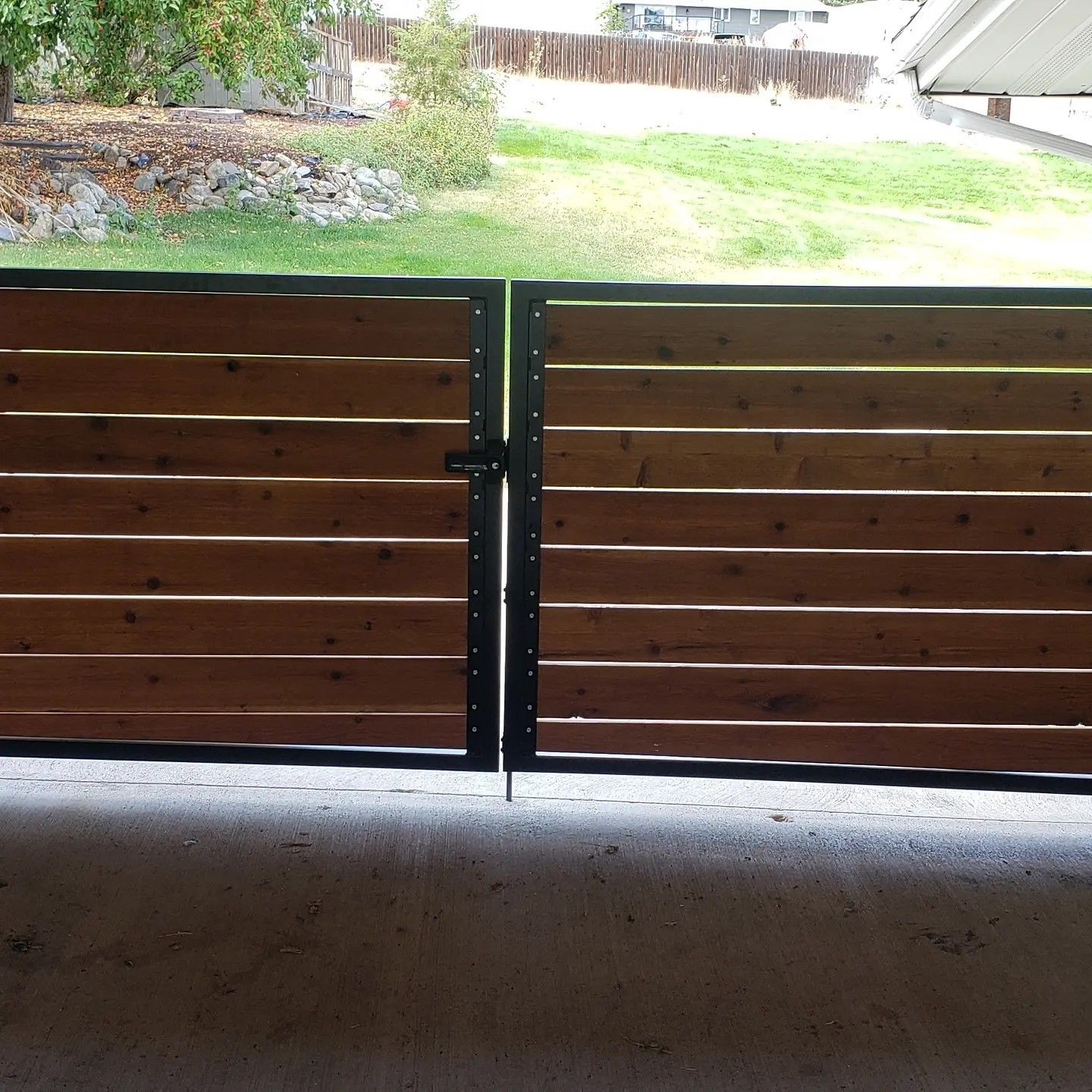 Wooden gate with horizontal slats and black metal frame, opening to a grassy yard.