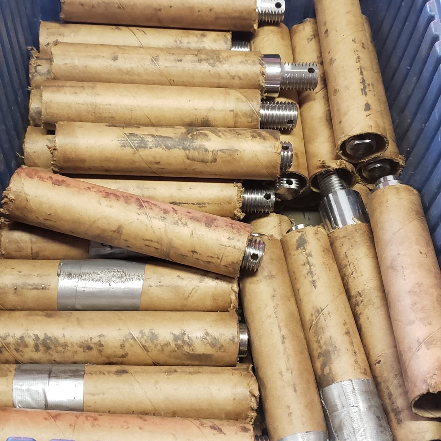 Metal cylindrical parts wrapped in brown paper, stacked in a blue bin.
