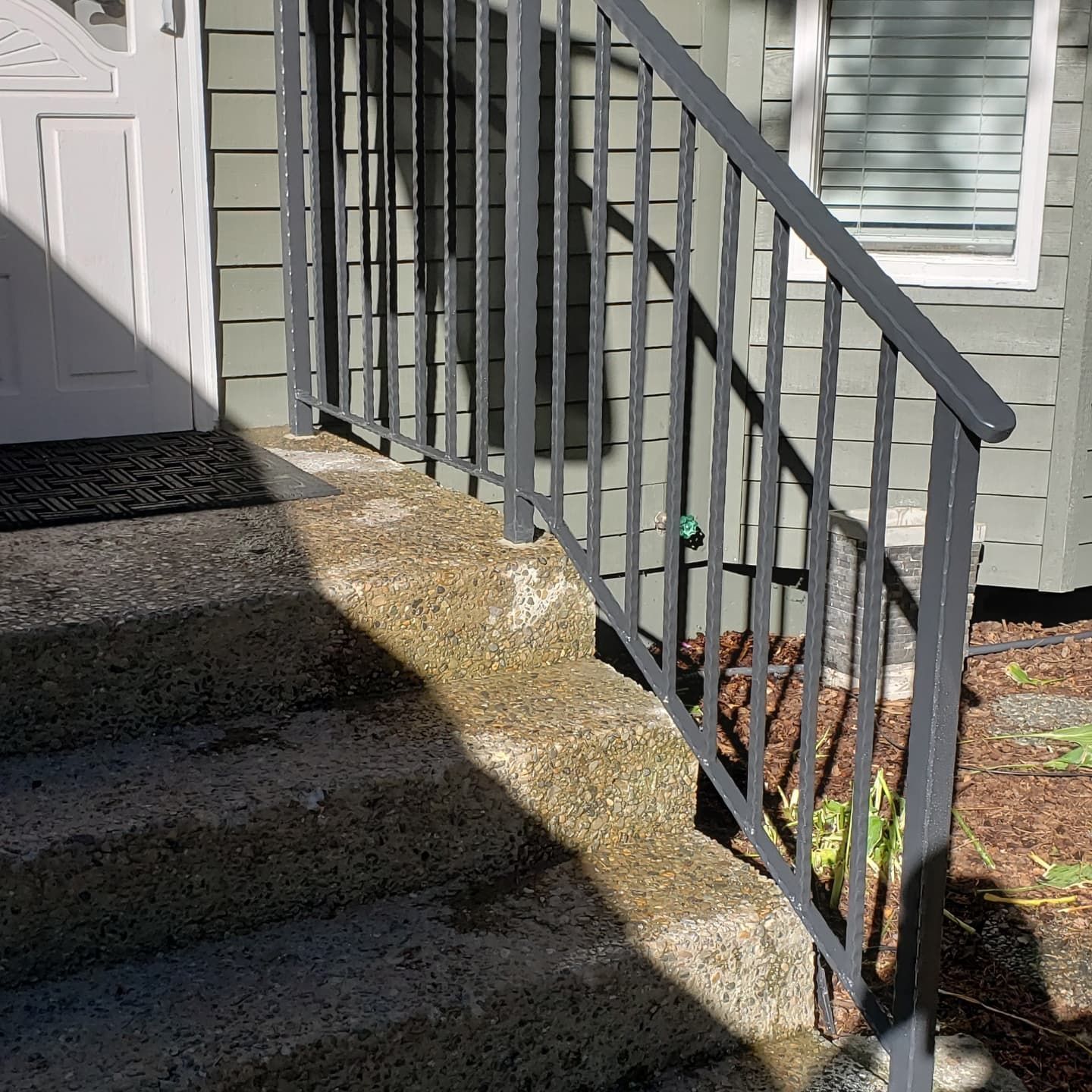 Gray metal railing on concrete steps leading to a door; green siding background.
