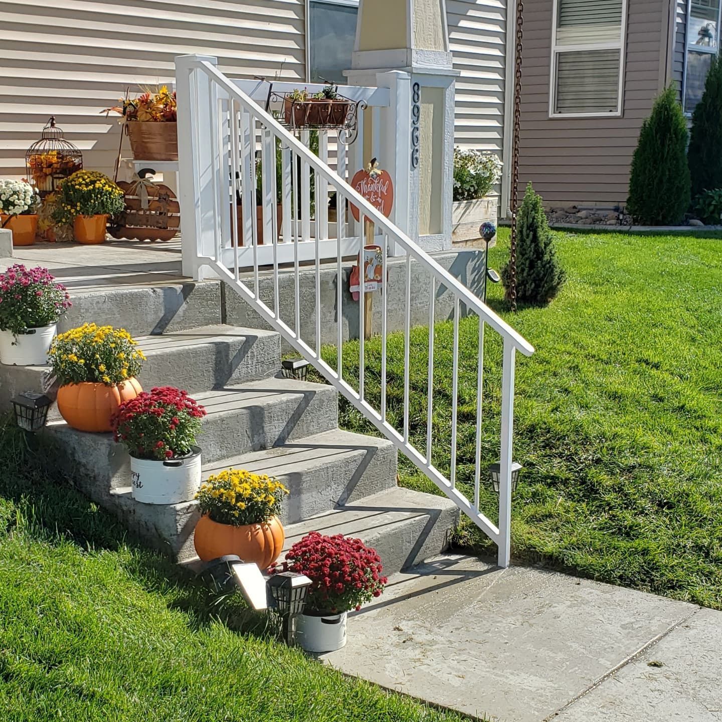 Concrete steps decorated with pumpkins and potted mums lead to a house with white railing.