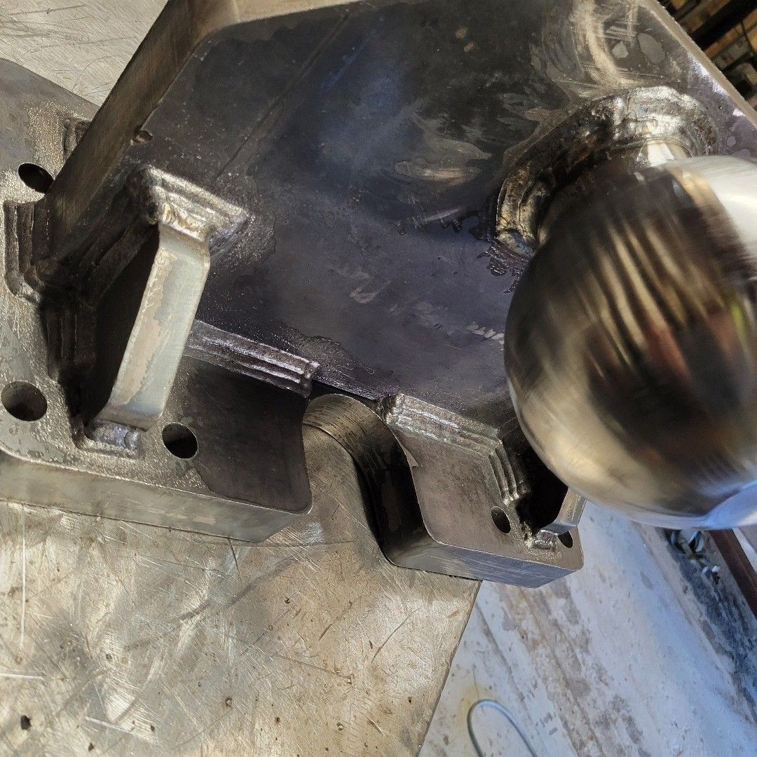 Close-up of a metal component with weld marks, featuring a curved section and a round metal ball.