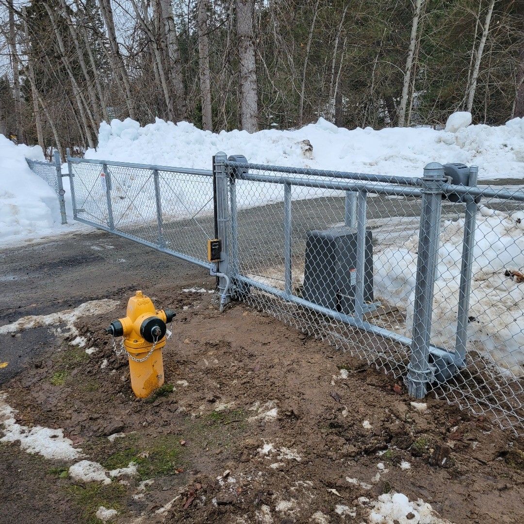 Yellow fire hydrant next to a chain-link fence gate, partially open. Snow on the ground.
