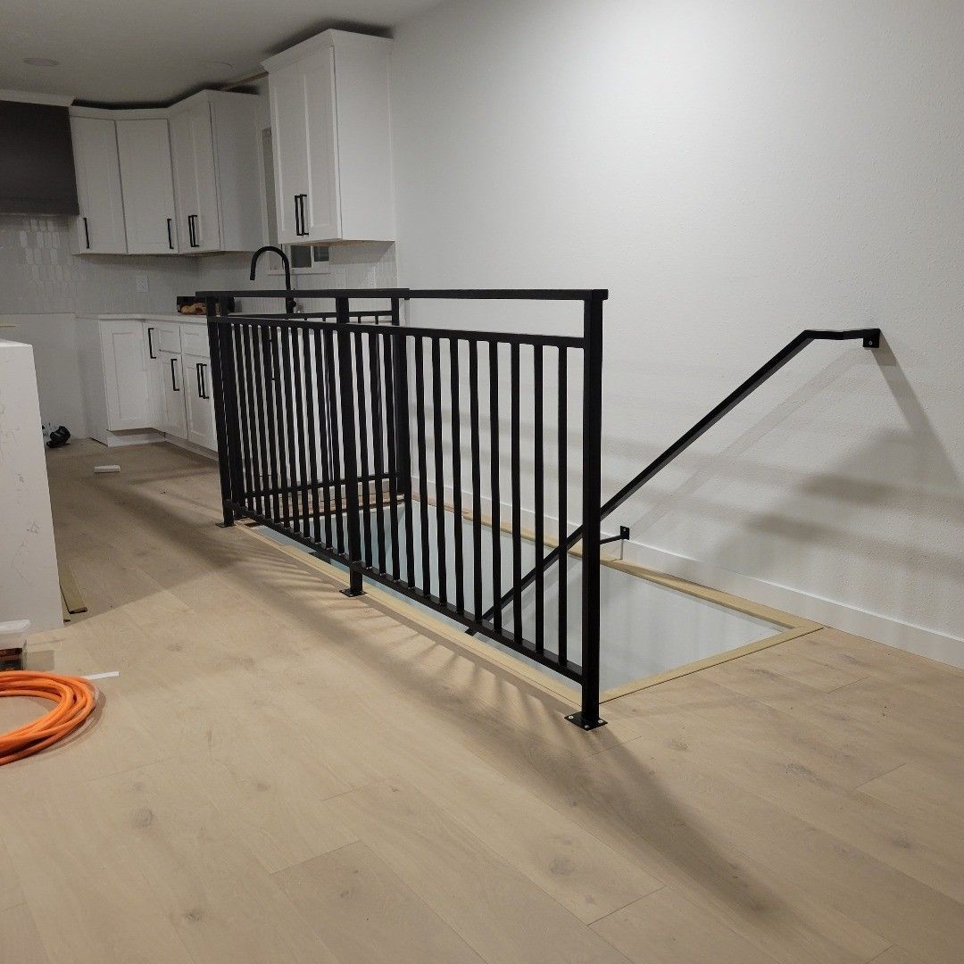 Black metal railing with a handrail to a lower level in a light wood floored room. White cabinetry is visible.