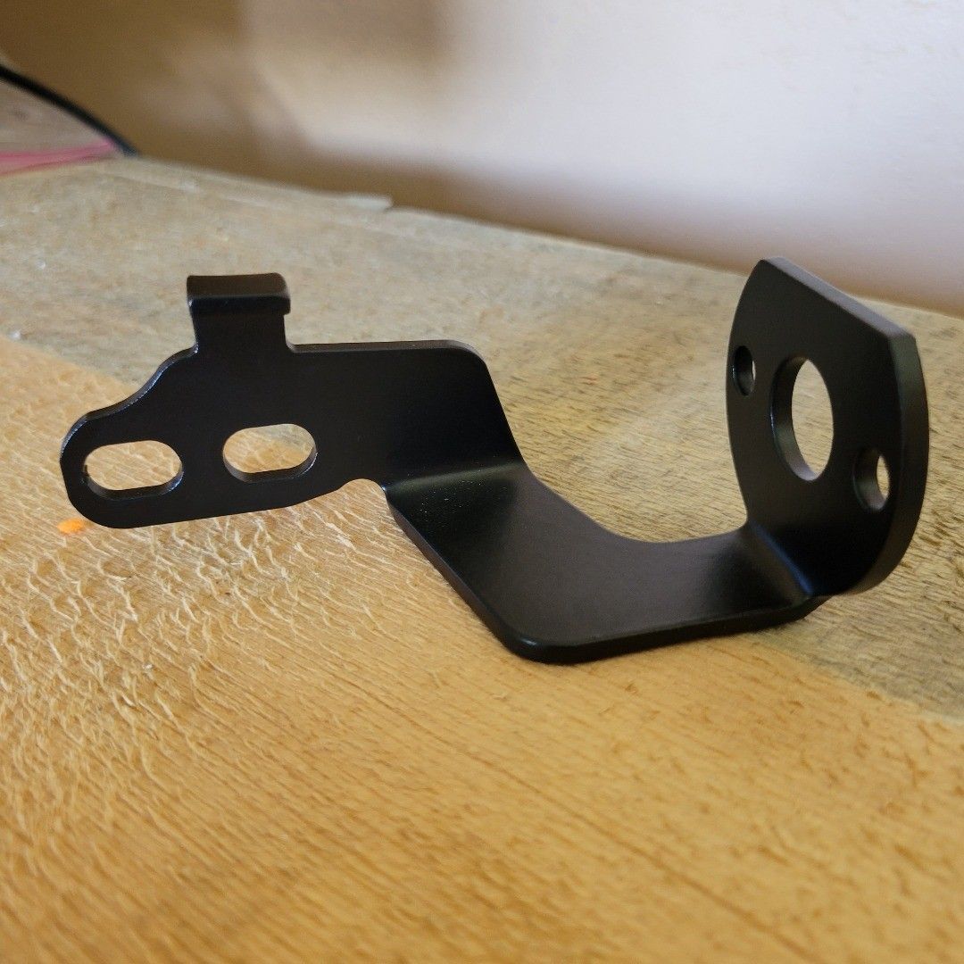 Black metal bracket with two elongated holes, a mounting tab, and a round hole.