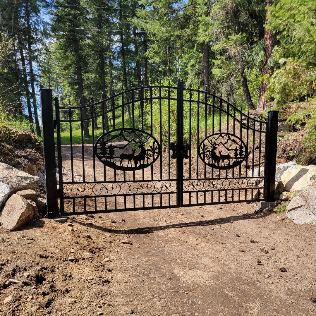 Black metal gate with oval silhouette of wildlife, between stone pillars, set in a forest.