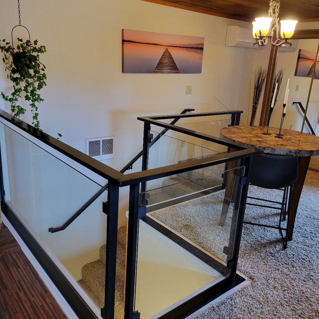 Staircase with glass railing, black frame, and carpeted steps leading down. A small table and hanging plant are visible.