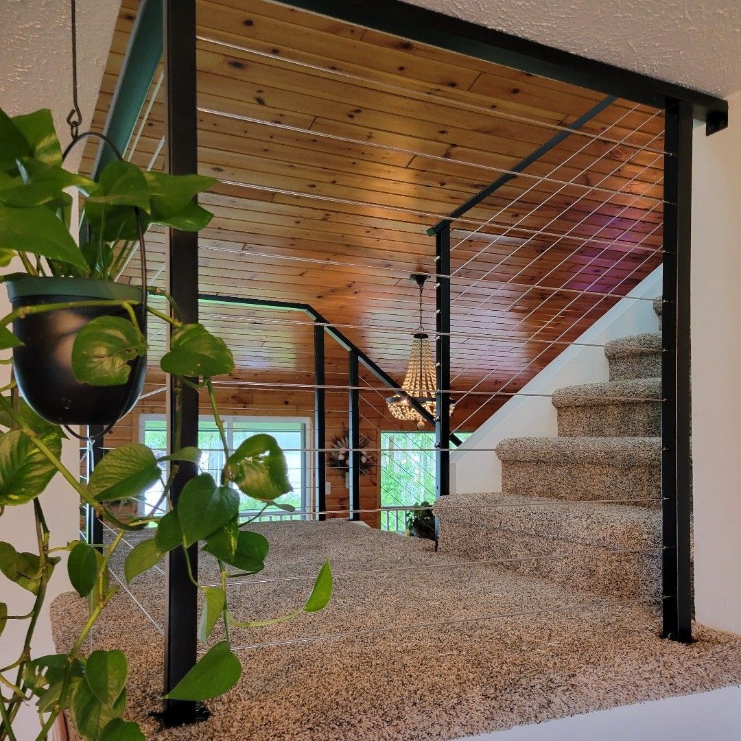 Staircase with carpeted steps, metal railing, and hanging plant. Brown wooden ceiling.