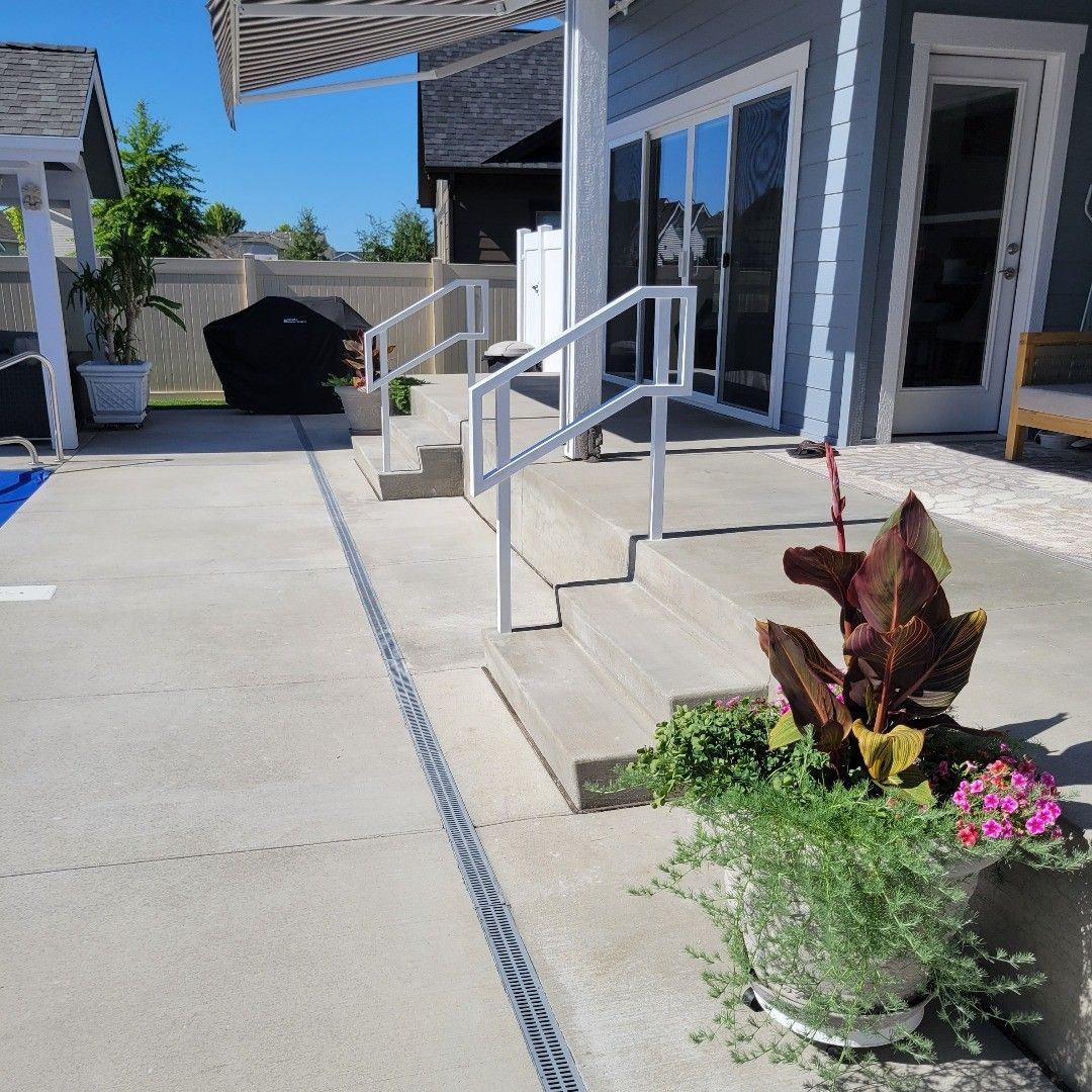 Concrete patio with steps, handrails, and potted plants next to a pool.