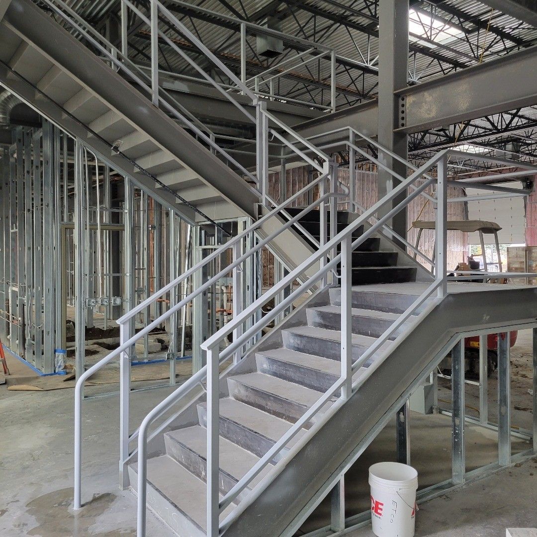 Metal staircase in an unfinished building, with gray steps and white railings.
