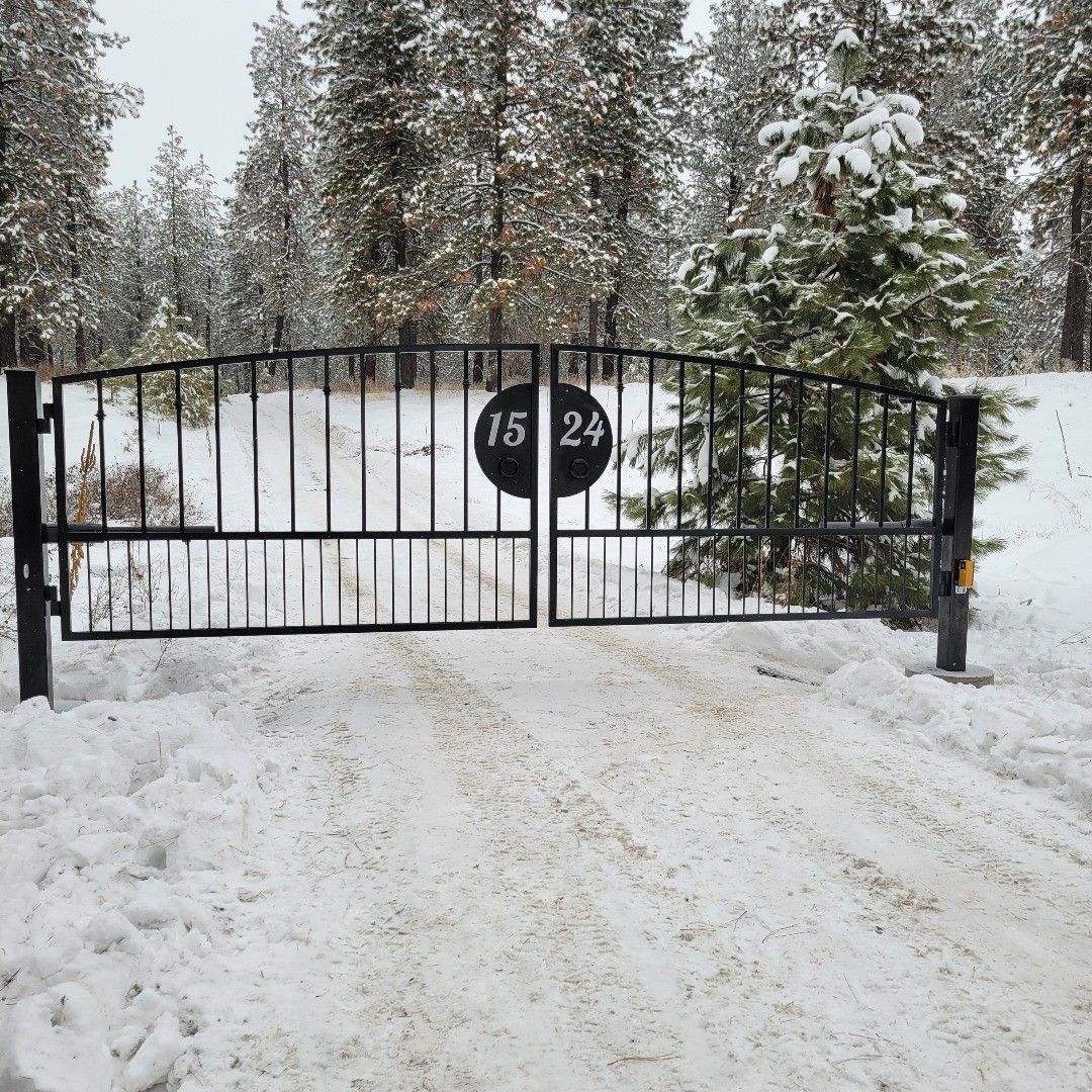 Black metal gate in snowy driveway, with house numbers 