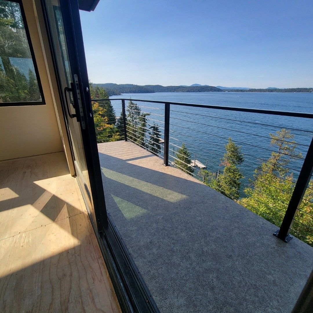 View from a cabin balcony overlooking a blue lake and forested shoreline under a sunny sky.