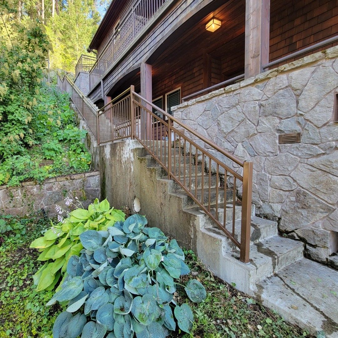 Stone and wood house exterior with stairs, greenery, and a balcony.