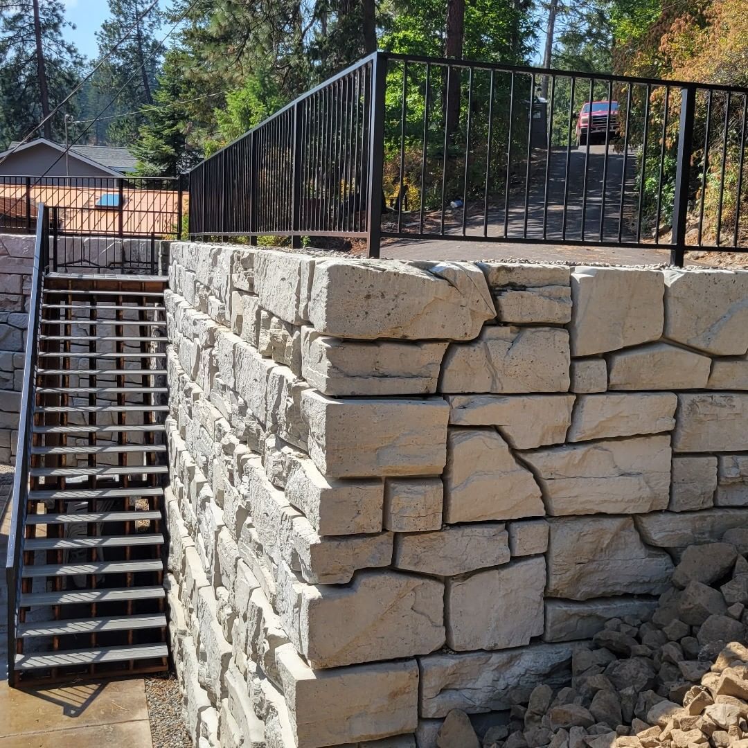 Stone retaining wall with metal stairs leading to a platform with a black metal railing.