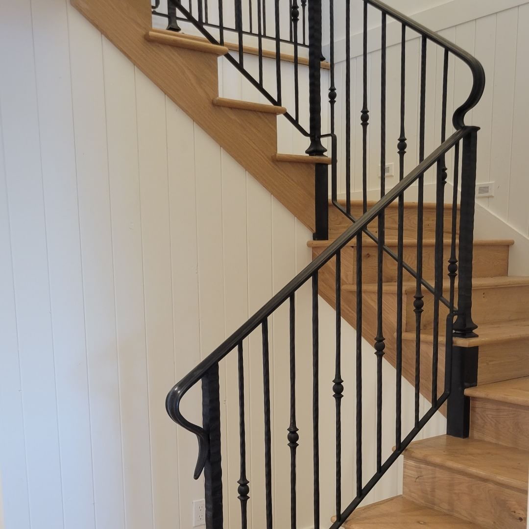 Wooden staircase with black metal railing and white paneled wall.