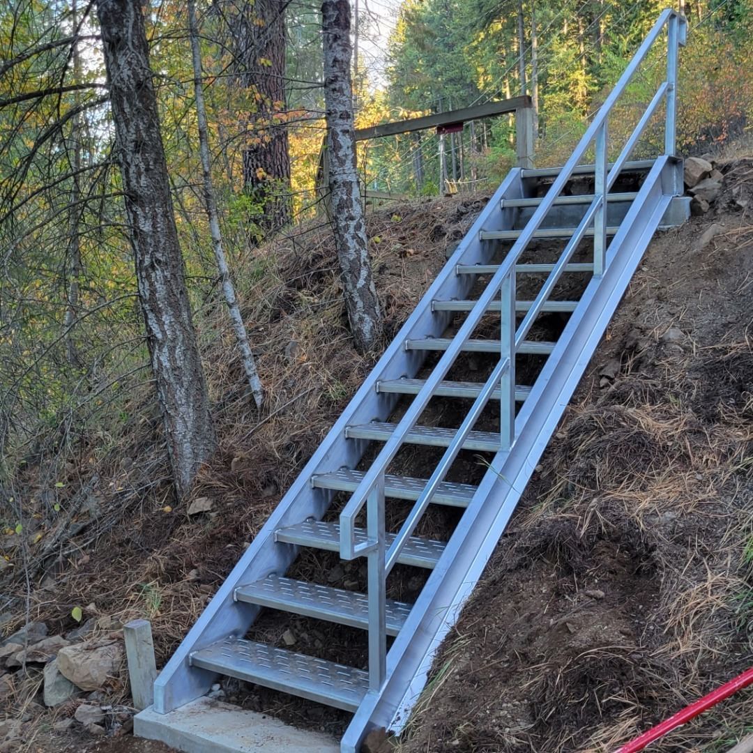 Metal staircase built on a hillside with handrails for accessibility in a wooded area.