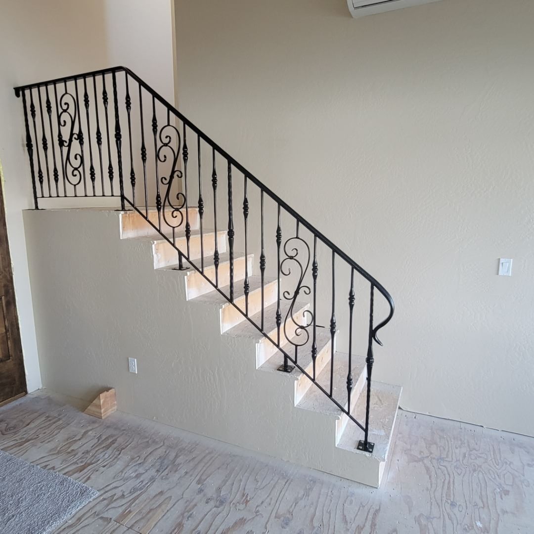 Staircase with black wrought-iron railing against a beige wall, leading upwards.