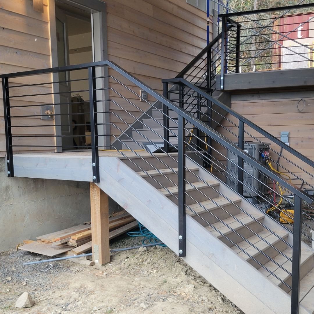 Exterior staircase with black metal railing and cable infill, leading to a wooden deck.