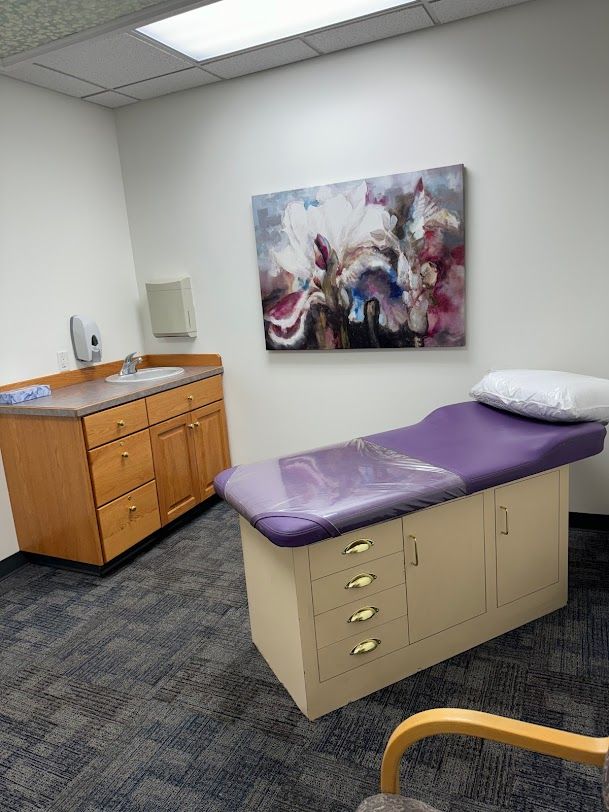 A doctor 's office with a purple bed and a painting on the wall.