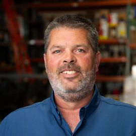 A man with a beard is wearing a blue shirt and smiling for the camera.