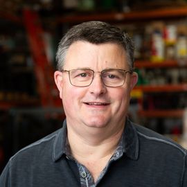 A man wearing glasses and a black shirt is smiling for the camera.