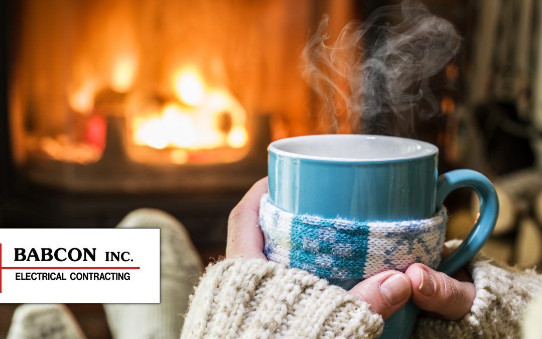 A person is holding a cup of hot coffee in front of a fireplace.