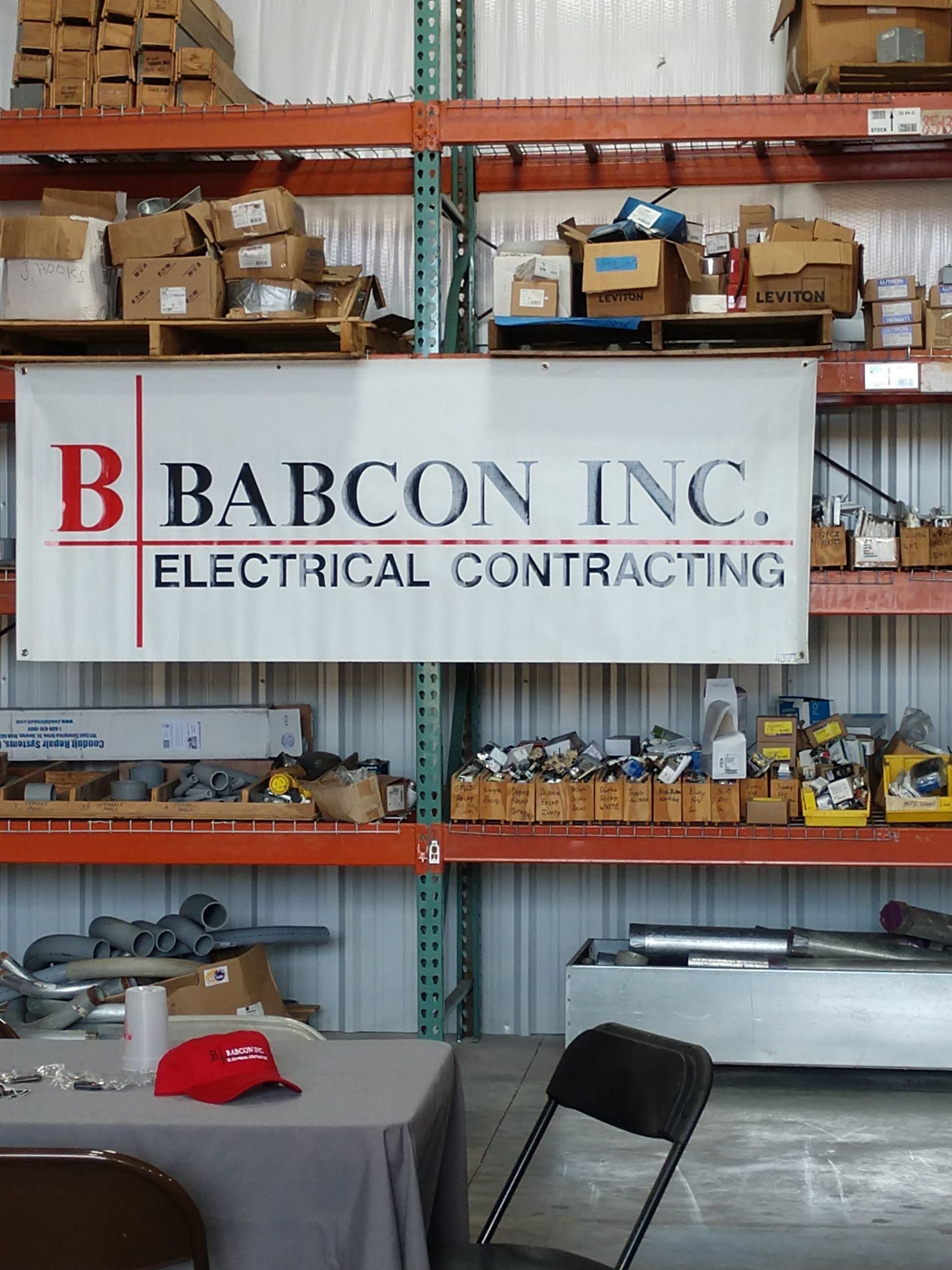 A sign for babcon inc. electrical contracting hangs above a table