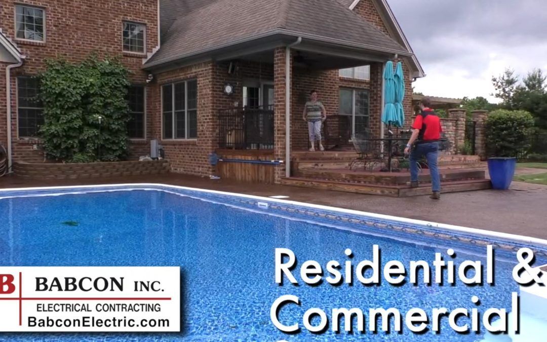 A man is standing next to a swimming pool in front of a brick house.