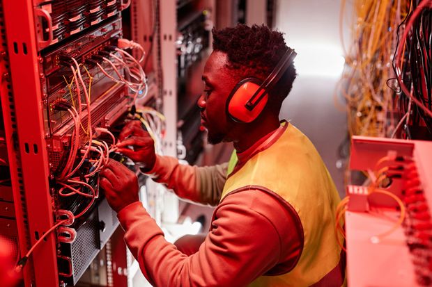 A man wearing headphones is working on a server in a data center.