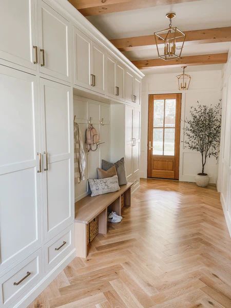 Hallway with white storage cabinets, wood bench, herringbone floor, and wooden door.