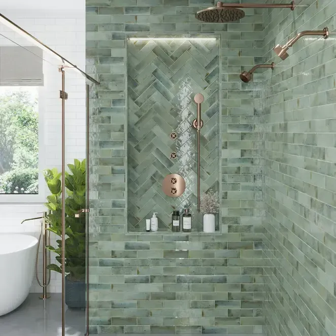 Green-tiled shower with a built-in shelf, copper fixtures, and a glass door, set in a modern bathroom.