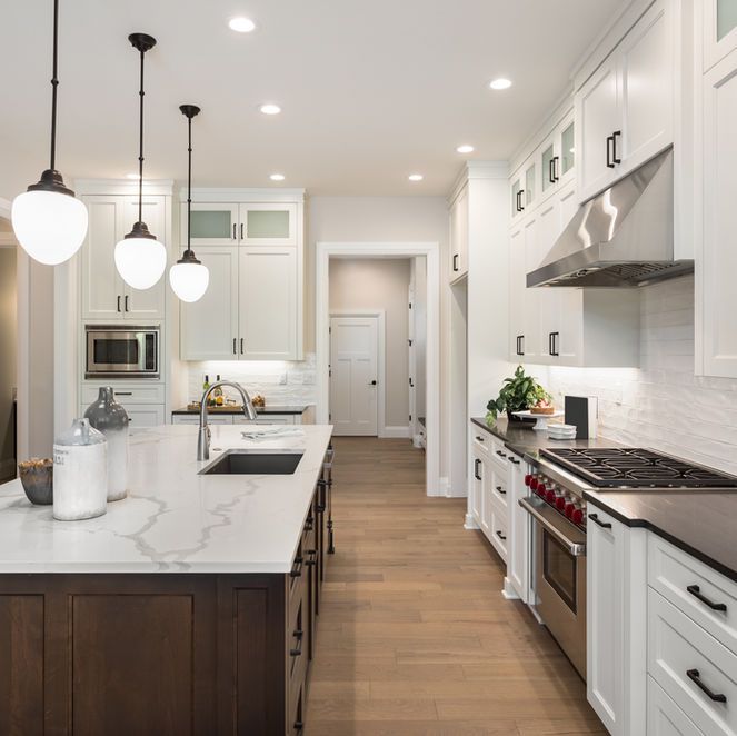 Modern white kitchen with a dark wood island, stainless steel appliances, and pendant lights.