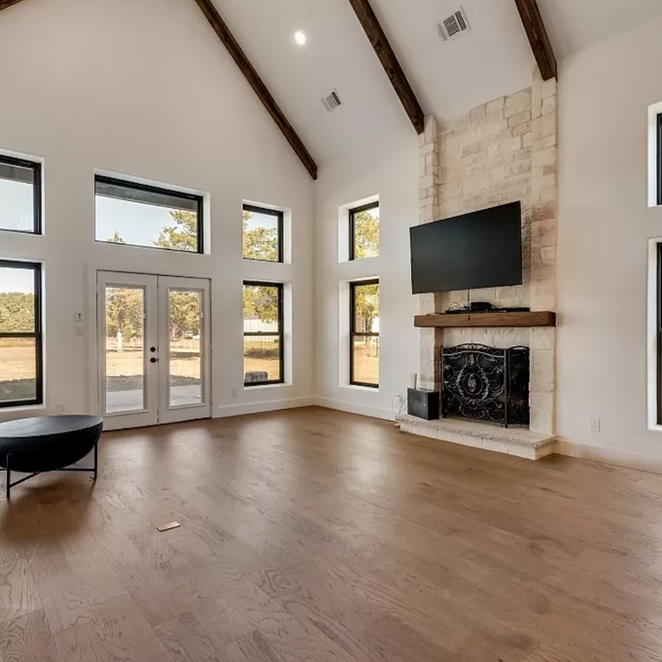 Spacious living room with high ceilings, fireplace, and large windows overlooking a field.