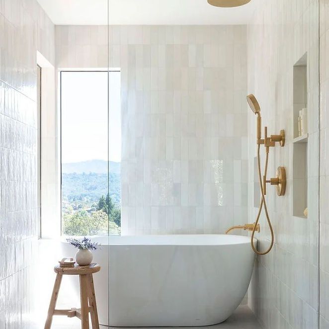 Modern white bathroom with a tub, gold fixtures, and a scenic window view.