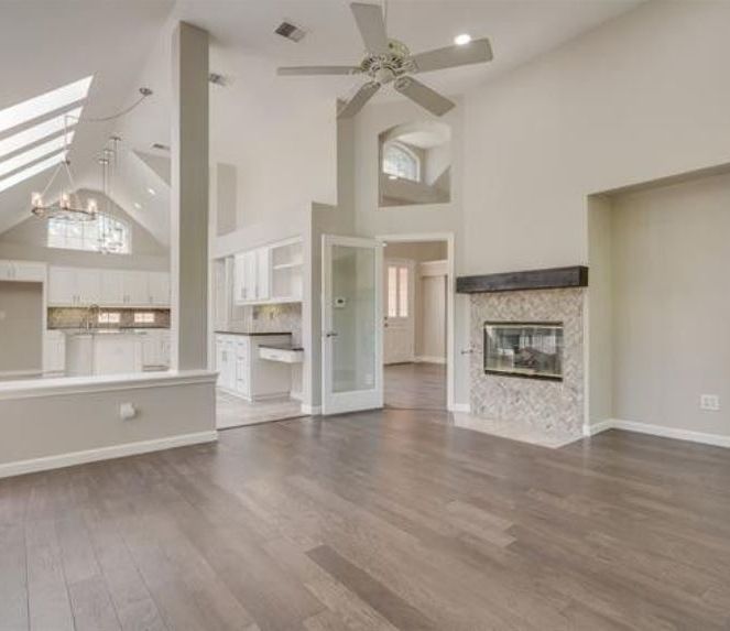Spacious living room with high ceilings, fireplace, and hardwood floors. Kitchen visible in the background.