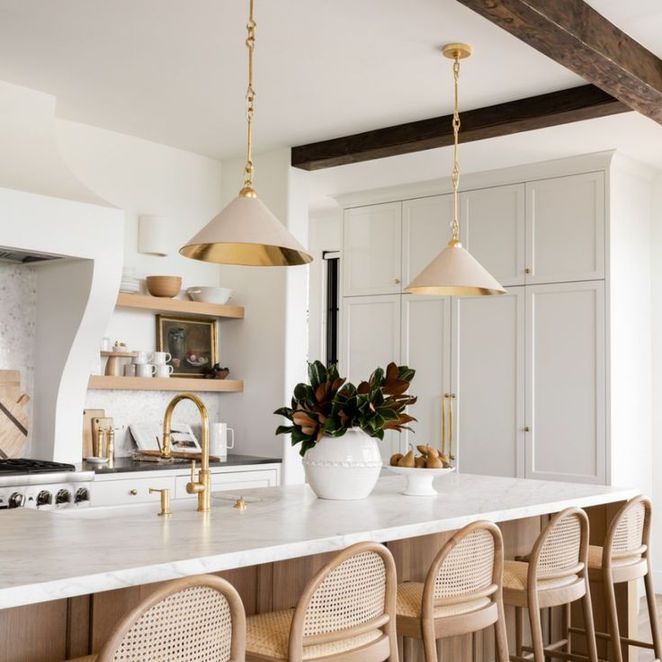 Kitchen with white cabinets, marble countertop, gold pendant lights, and rattan bar stools.