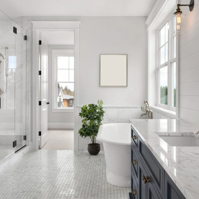 Elegant white bathroom with marble tile, dark blue vanity, and a freestanding tub.