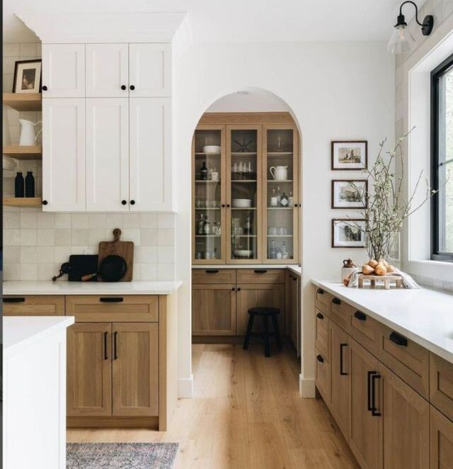 Kitchen with light wood cabinets, white upper cabinets, and a pantry with arched entry.