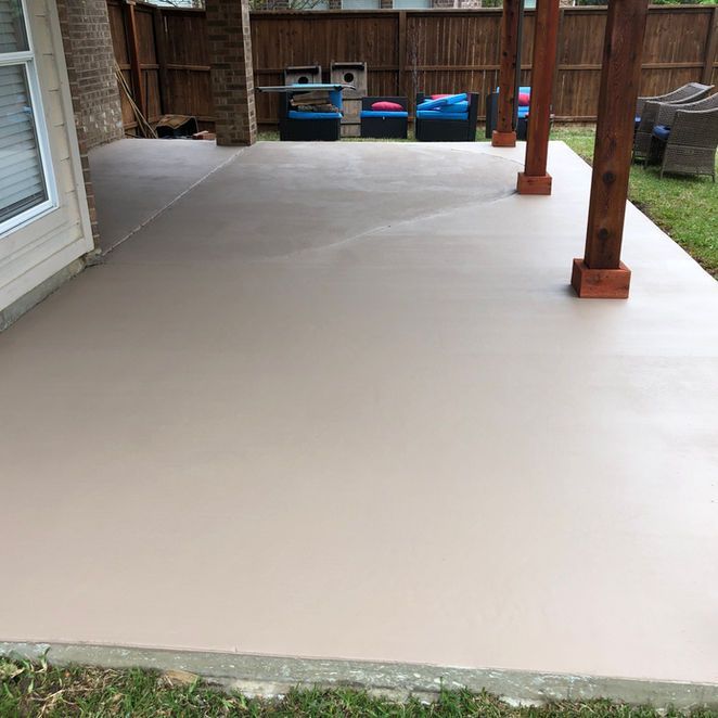 A light-colored concrete patio with wooden support beams and a partial pergola in a backyard.