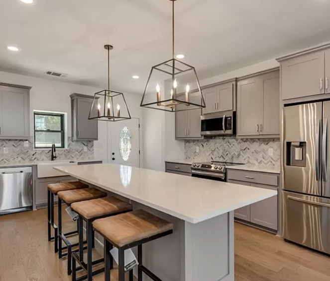 Modern kitchen with gray cabinets, white countertops, island with stools, and pendant lights.