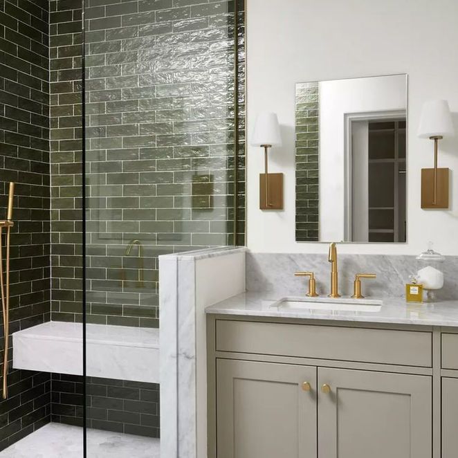 Bathroom with dark green tiled shower, gray vanity, gold fixtures, and a marble countertop.