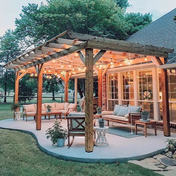 Patio with pergola, string lights, and seating near a house with glass doors.