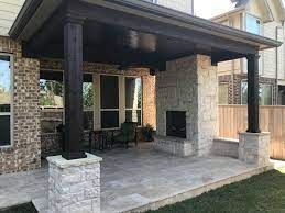 Covered patio with stone fireplace, dark columns, and tile flooring.