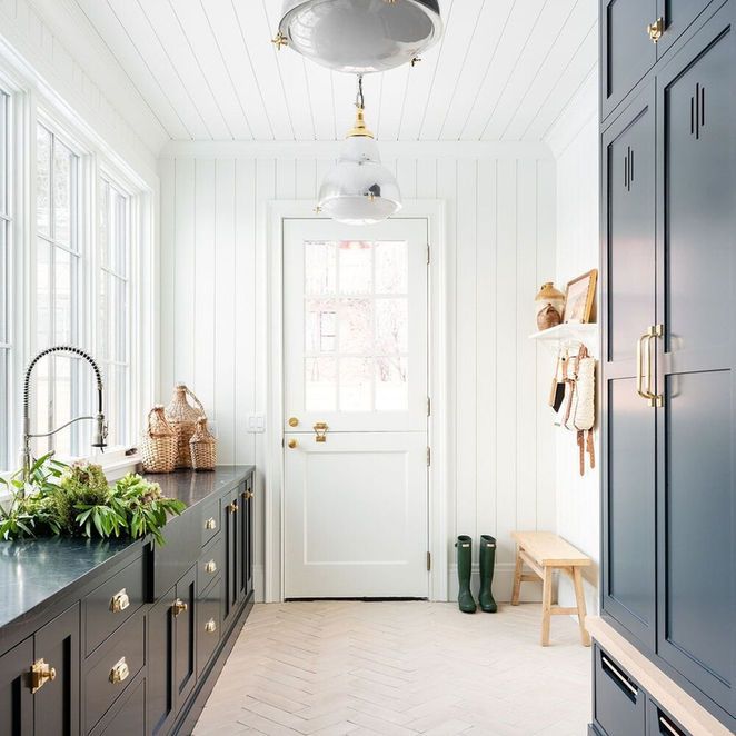 A bright, white laundry room with dark blue cabinetry, white door and ceiling, and wooden floors.