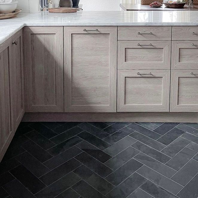 Kitchen cabinets with marble countertop and herringbone pattern dark tile floor.