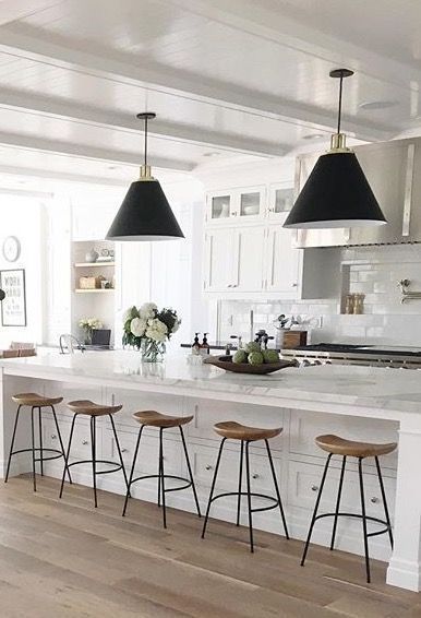 Kitchen with white cabinets, island, black pendant lights, and wood stools.