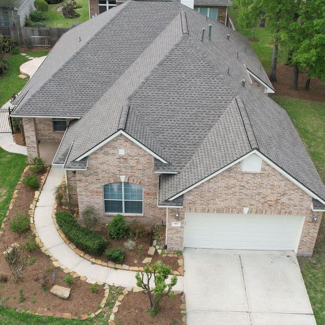 A brick house with a gray roof, driveway, and landscaped yard.